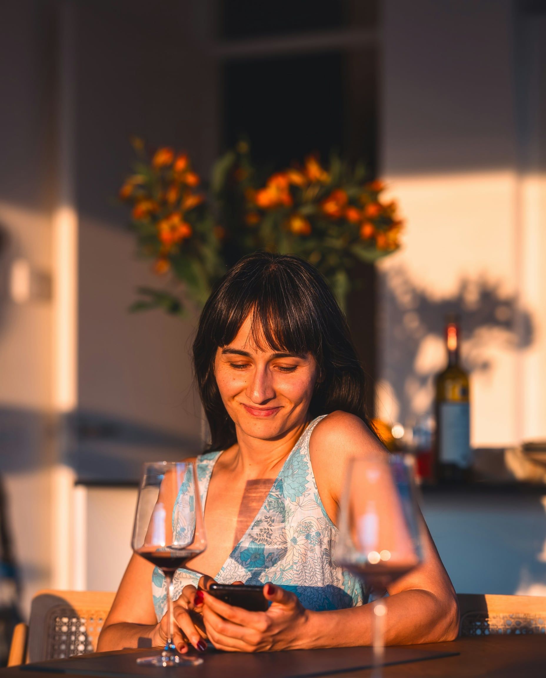 A member smiling at her phone over a glass of red wine